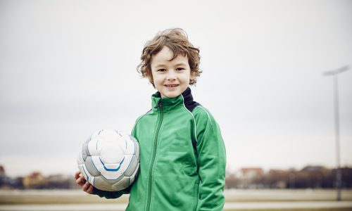Boy holding football looking at camera smiling