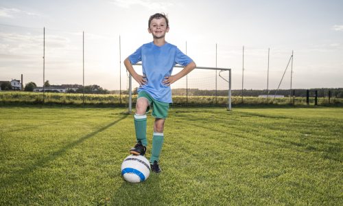 Portrait of confident young football player with ball on football ground