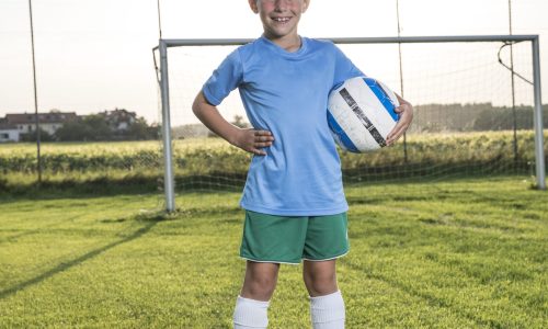 Portrait of smiling young football player holding ball on football ground